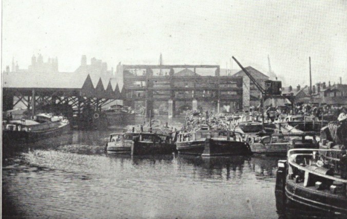 Busy canal wharf scene with barges loading and unloading