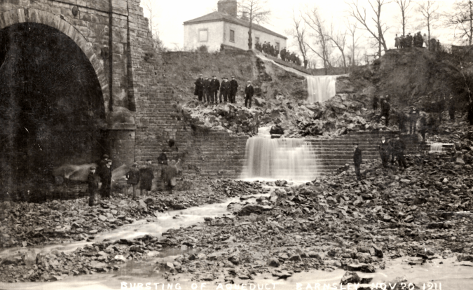 Photographic postcard of the burst abutment of the aqueduct of the Barnsley Canal, with spectators viewing the damage as water pours down the breached stone.