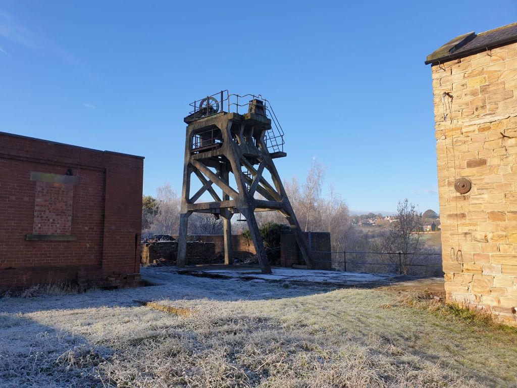 Bright light and dark show in the frosty grass yard at Hemingfield Colliery, photograph looking towards the concrete headgear of the main winding shaft. A bright blue sky behind the headgear.