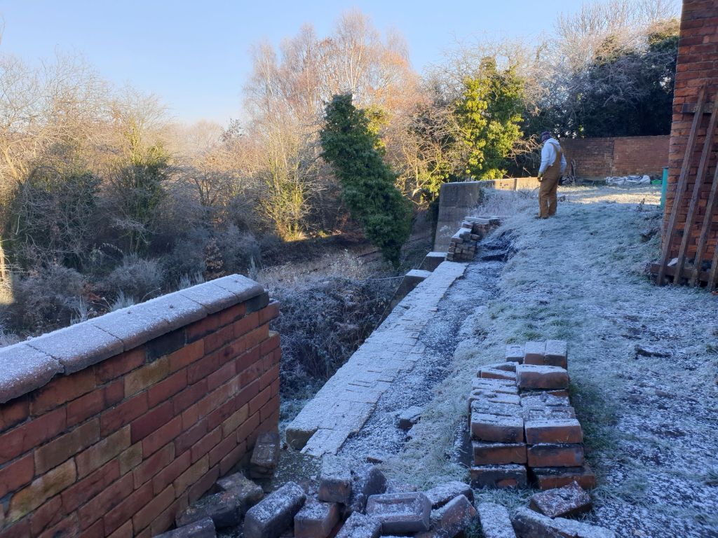 frosty-snow covered ground and wall at the rear of the winding engine house at Hemingfield Colliery, with a warmly wrapped volunteer surveying the scene