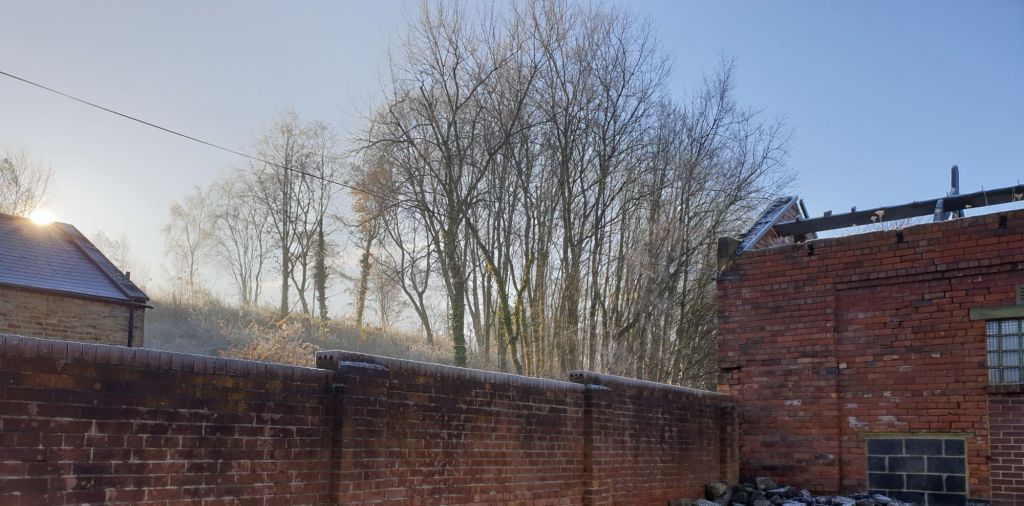 Photograph of the bright sun piercing through the frosty air above the roofline of Pit Row across into the yard at Hemingfield Colliery