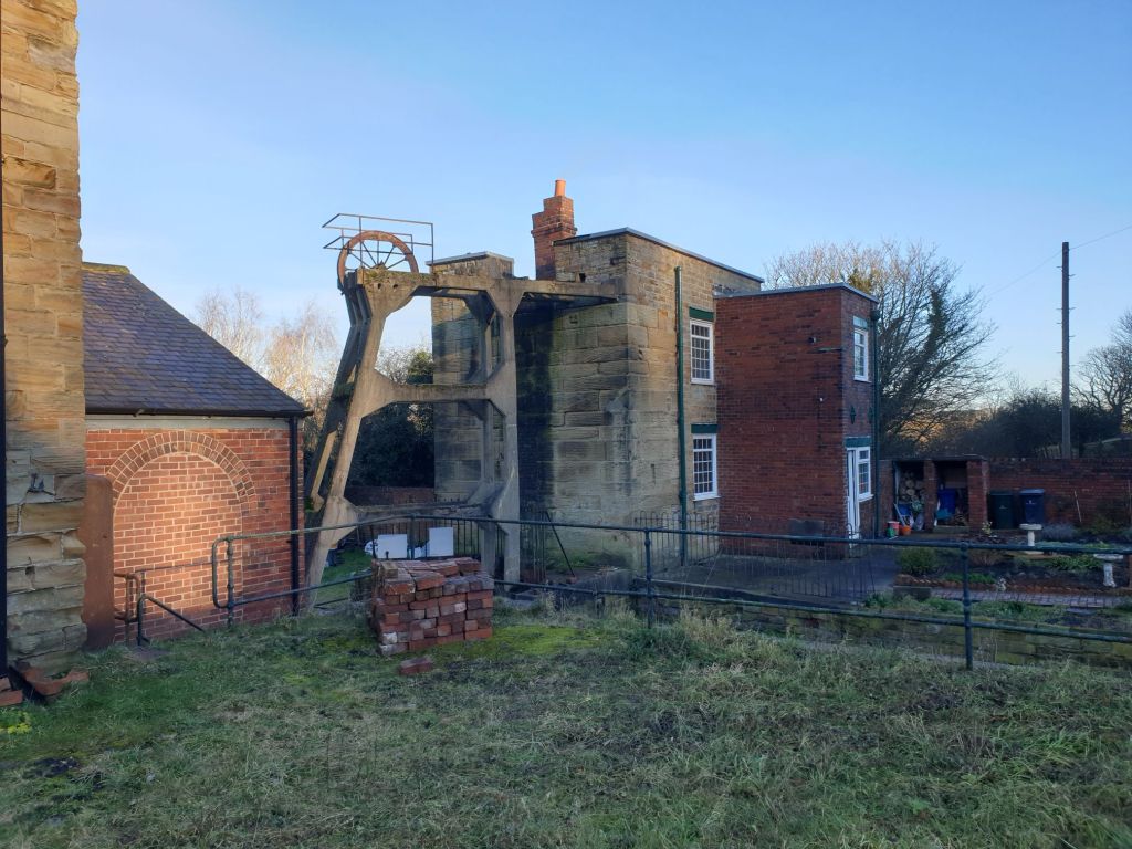 View across to Pump House Cottage and water shaft, with a pile of bricks in the foreground, freshly moved in preparation for future repair use at the rear of the site,